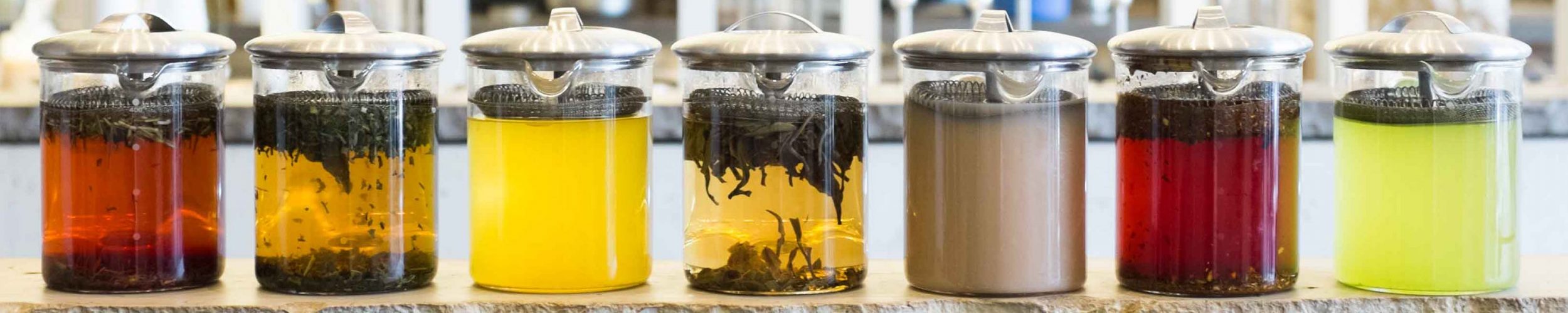 Seven different teas being brewed in glass teapots